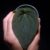 Anthurium Kunayalense with three round, wide, heart-shaped velvet leaves in deep dark green, featuring prominent deep red primary veins and a red sinus, pronounced muscular leaf texture, and subtle secondary venation. Plant displayed in a transparent pot held mid-air by a hand, captured in top-down lighting with a clean dark background highlighting the leaf texture, venation, and distinctive shape.